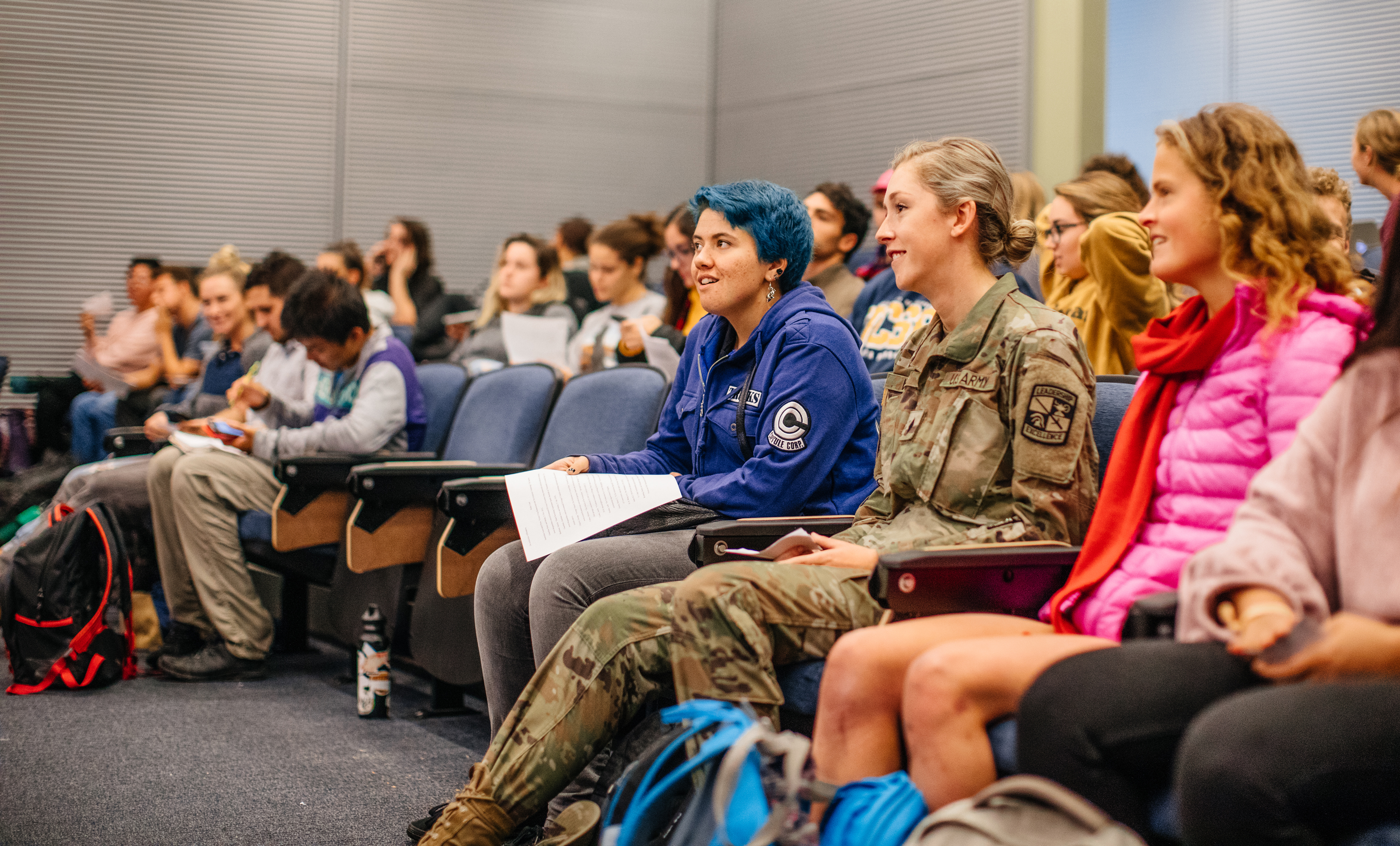 A woman in a U.S. Army uniform sitting in a lecture hall full of students