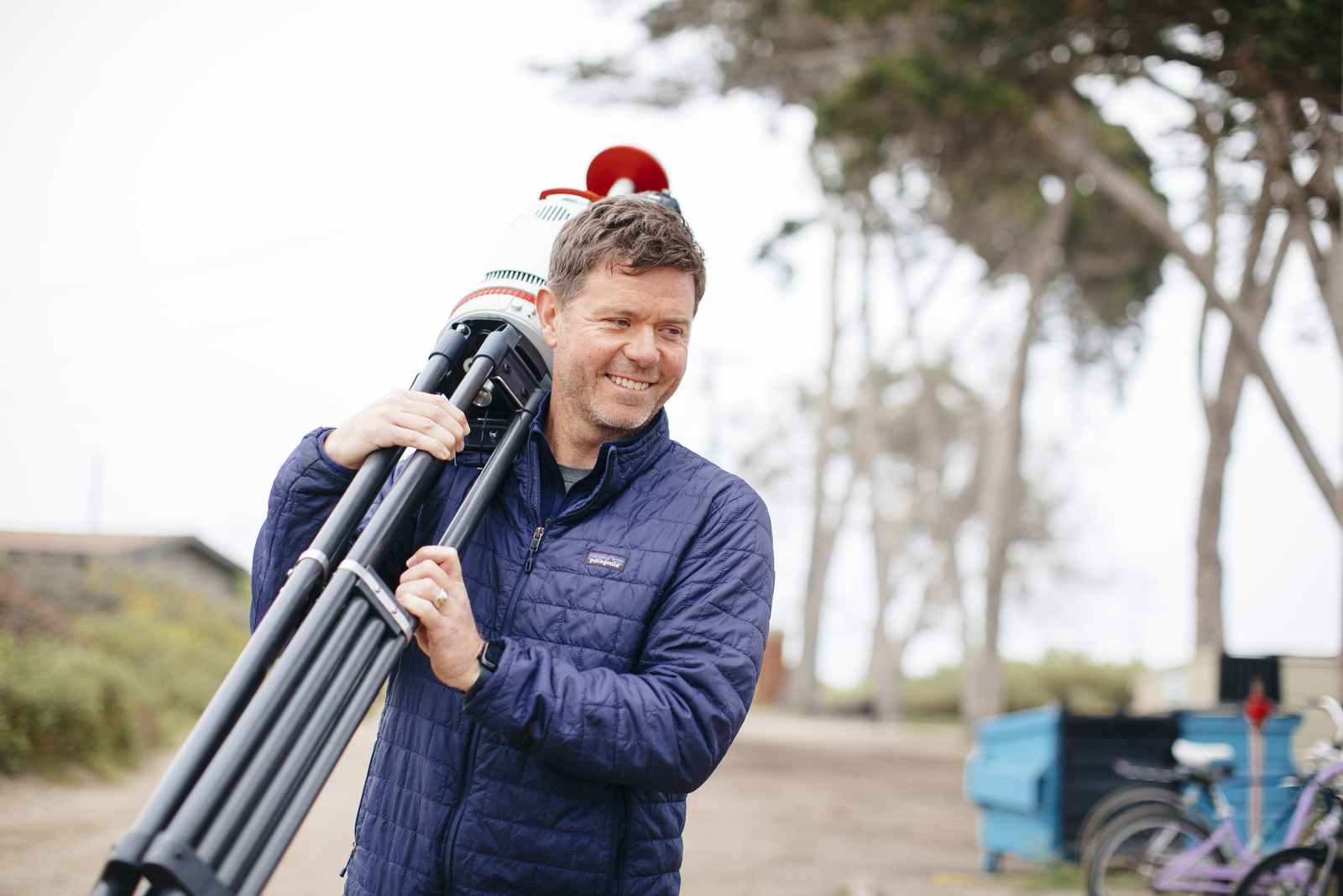 Ian Walker carries a hefty tripod on a coastal trail on a cloudy day