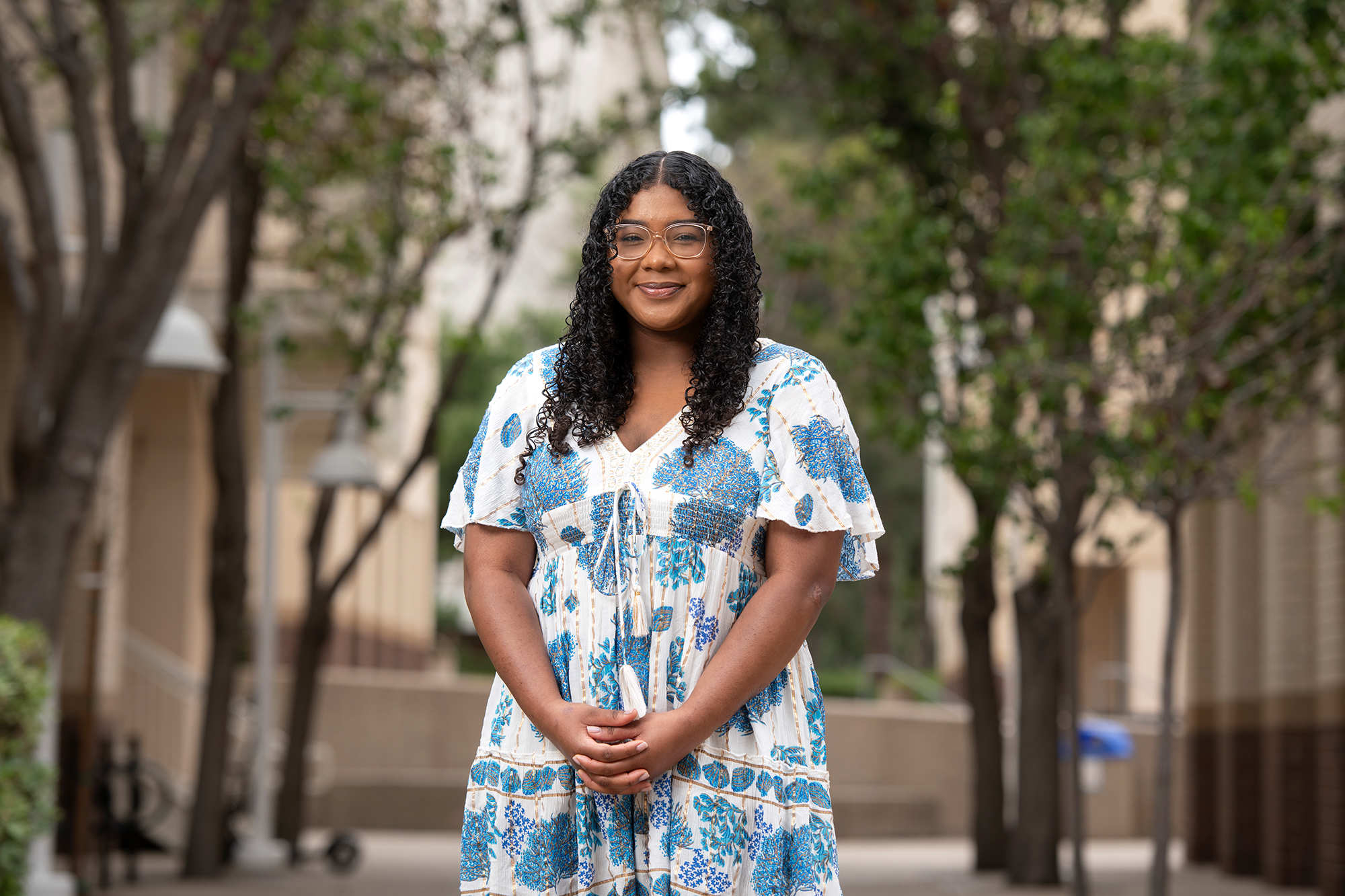 Young woman in blue and white dress poses outside, smiling