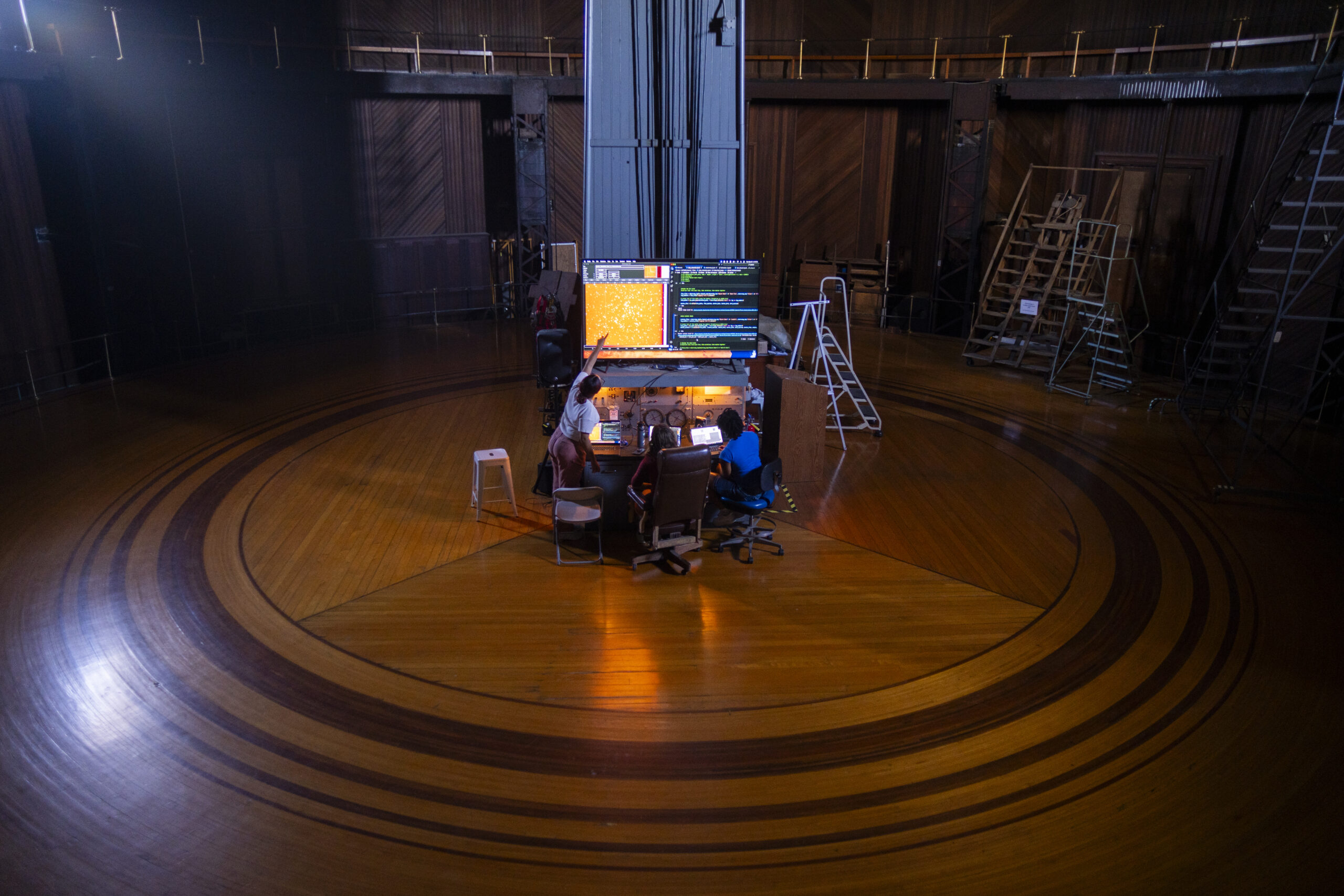 A tall, complex machine in the middle of a room with a circular design in its wooden flooring.