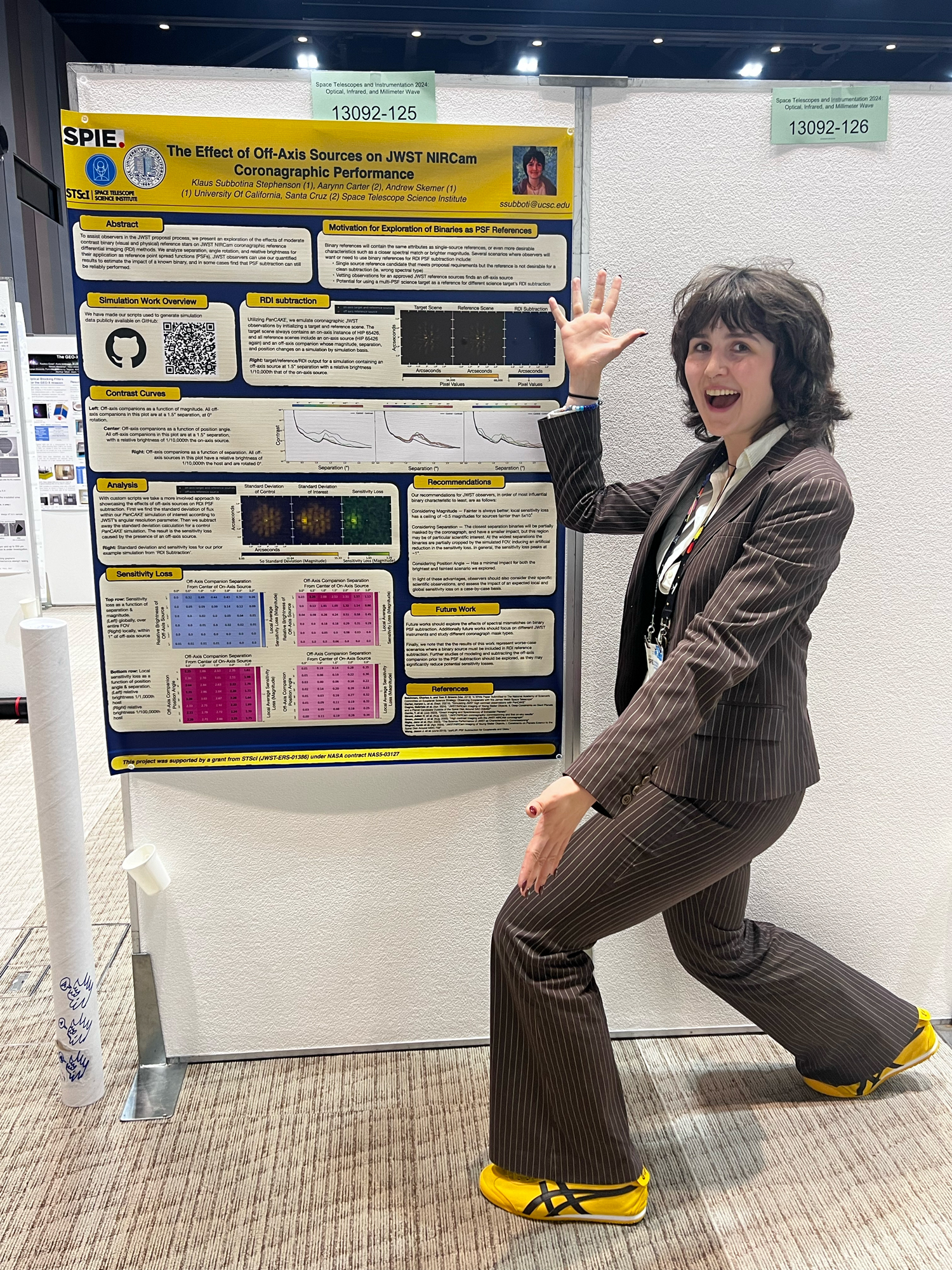 A young woman with a bob in sneakers and a suit throws up her hands dramatically at a poster
