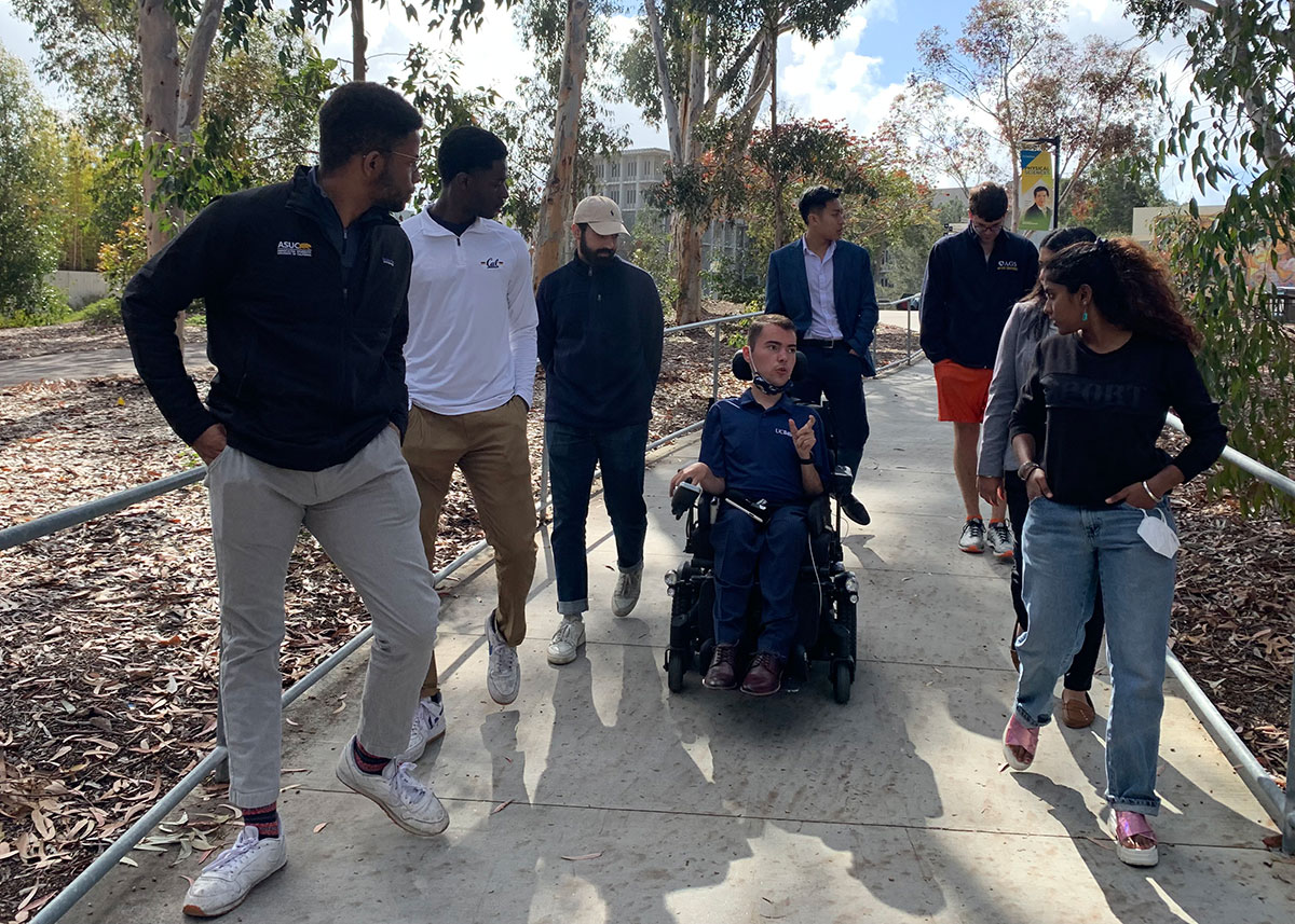 Ryan Manriquez at the center of a group of UC 8 students traveling down a sidewalk on campus. Other members of the group listen attentively while Ryan speaks.