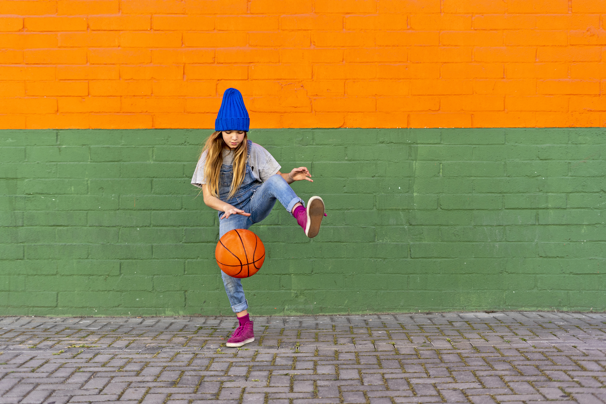 A girl bouncing a basketball against a colorful wall
