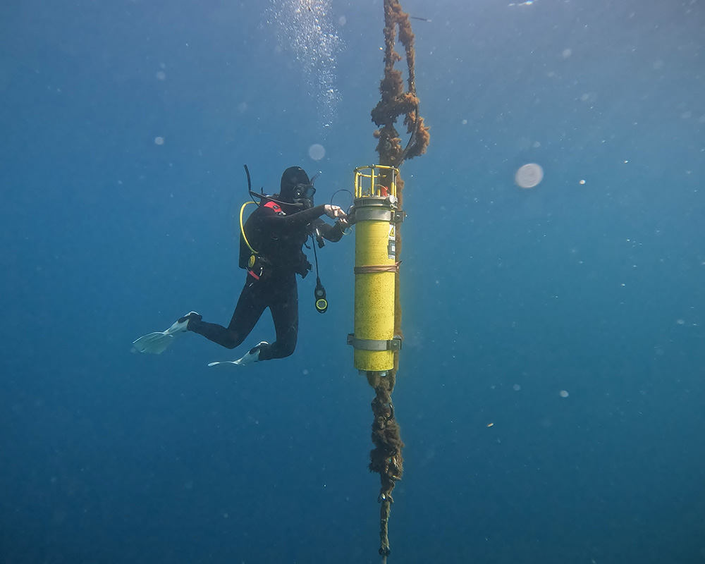 A SCUBA diver floats next to a yellow columnar instrument underwater