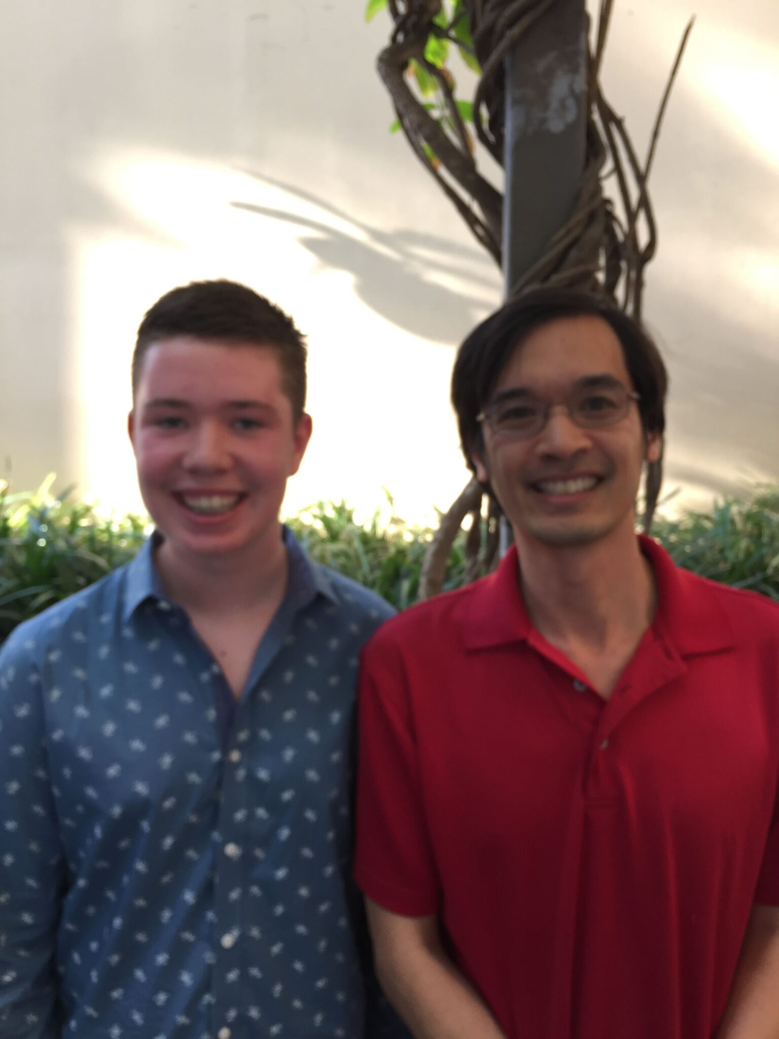 a boy in a collared shirt smiles next to a man in glasses and a red polo