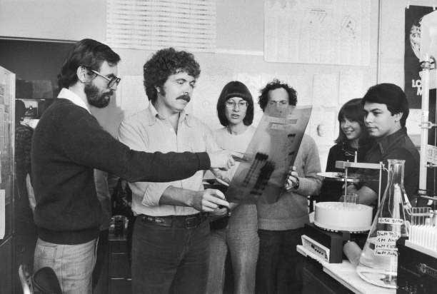 A black and white photo of several people pointing at a medical image in a lab in the 60s