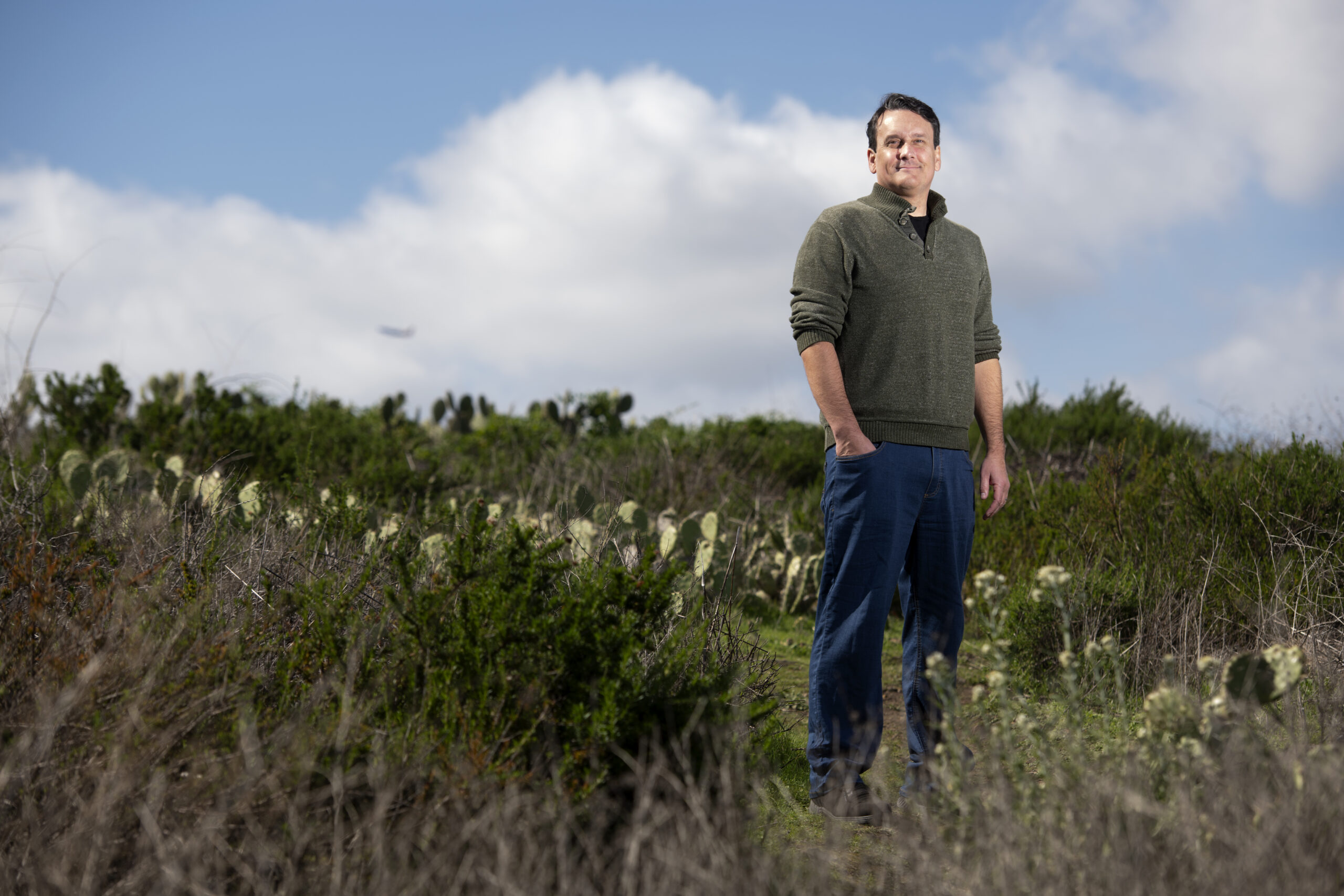 Bill Tomlinson, wearing jeans and a sweater, stands in a field