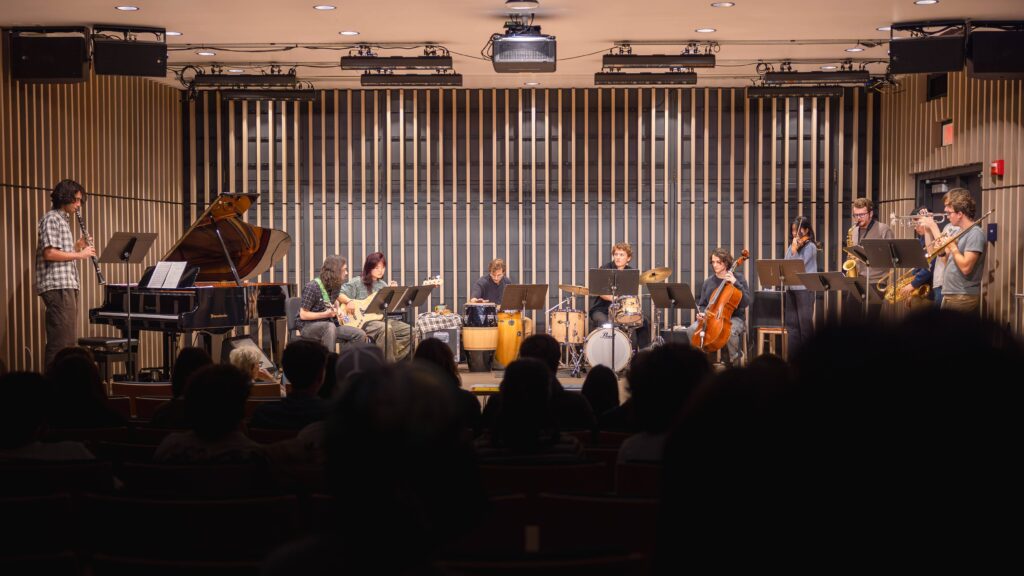 A dozen musicians on stage in a performance hall