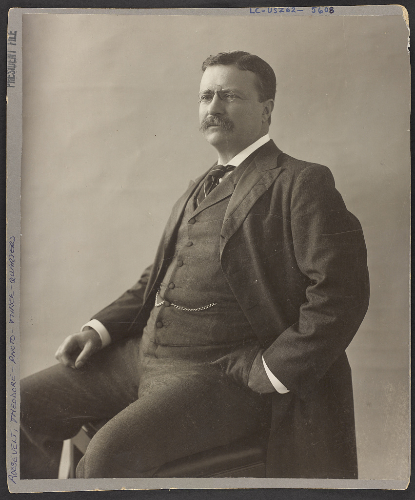 A black and white portrait of President Teddy Roosevelt, seated