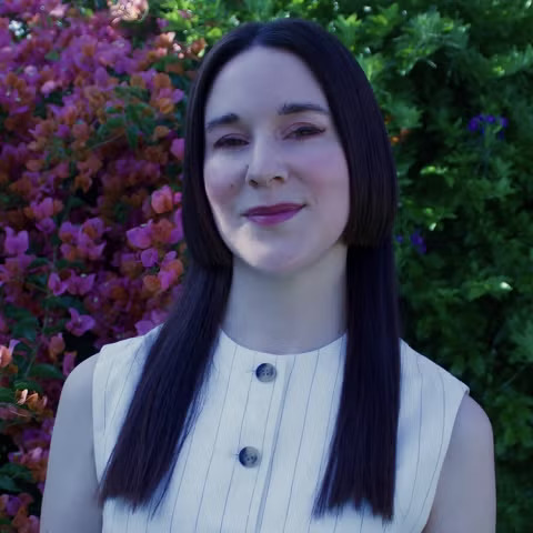 Woman with long dark center-parted hair smiles outdoors