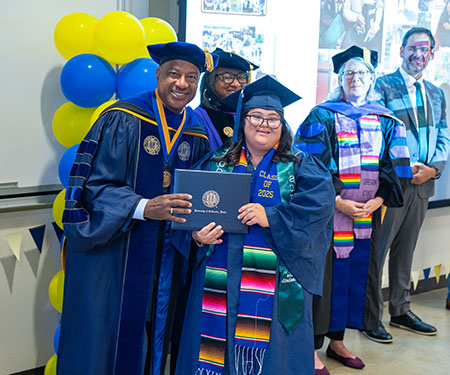 A graduating student holds her degree, posing with the chancellor