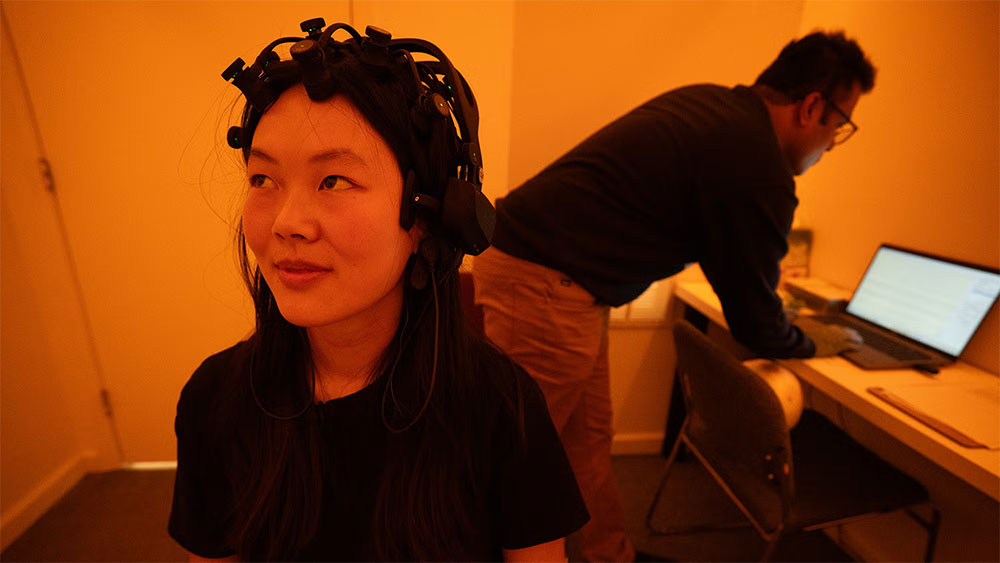 A student wearing a measuring device on her head sits in a lab bathed in amber light