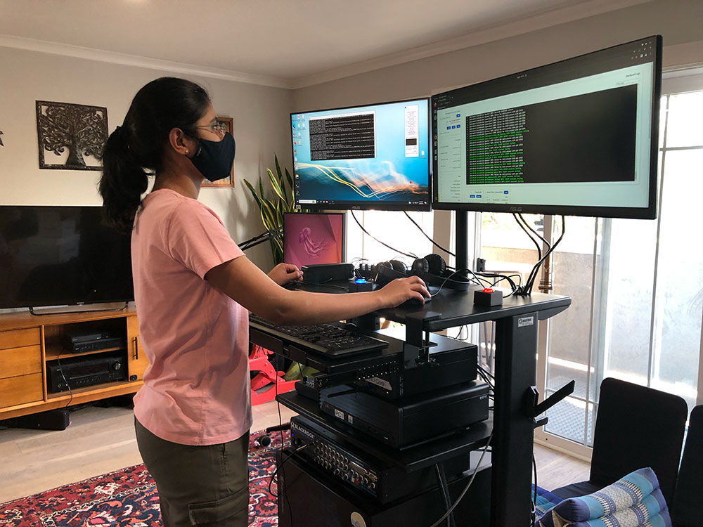 Maitreyee Wairagkar uses a computer with 2 monitors at a standing desk in a living room.