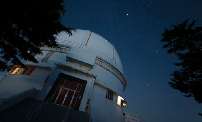 The exterior of an observatory at night, with stars shining above