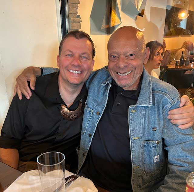 Two men smiling with hands around each other's shoulders at a restaurant