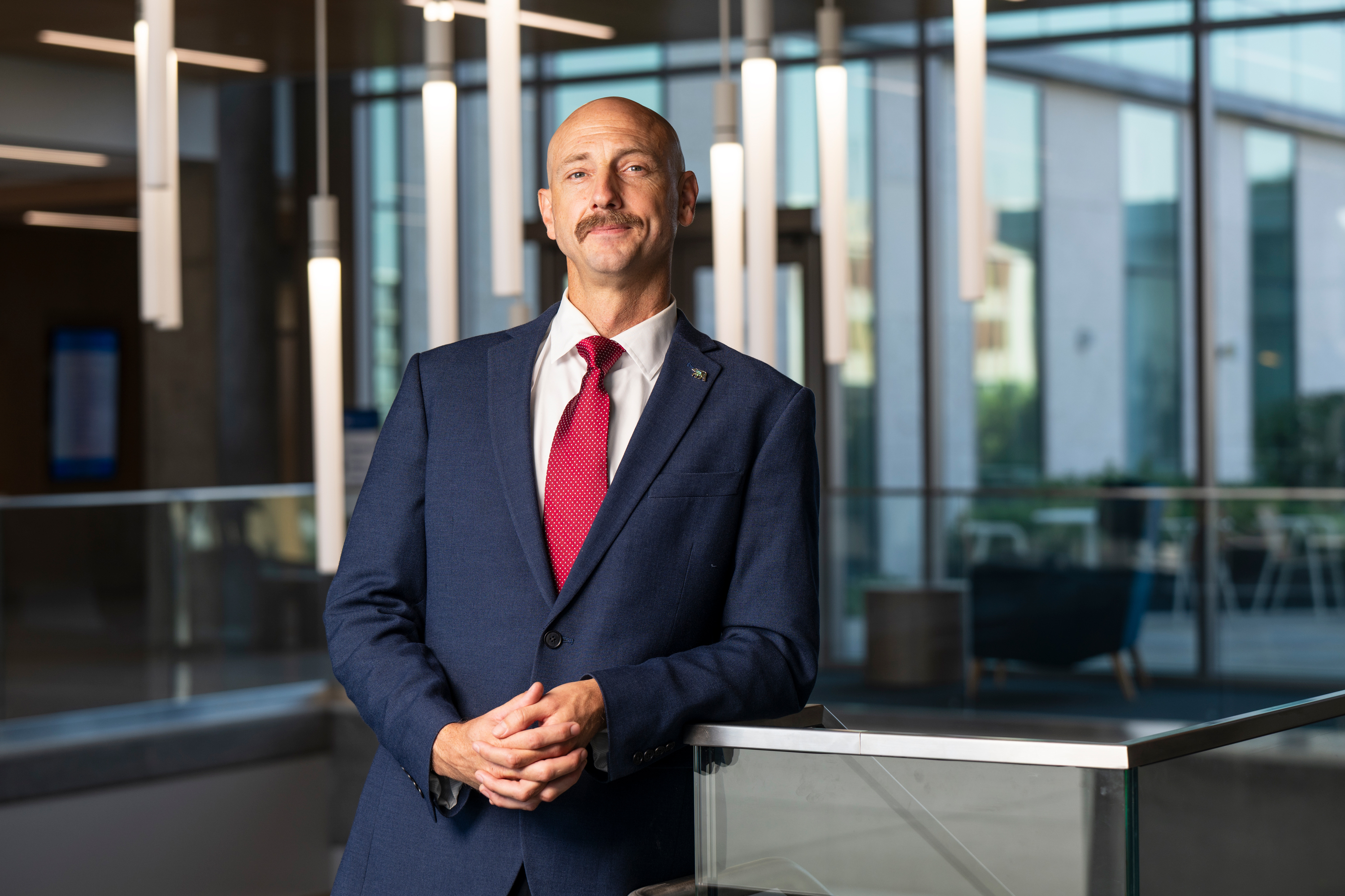 Harwood Garland wearing a blue coat and red tie in a glass-walled building on the UC Irvine campus
