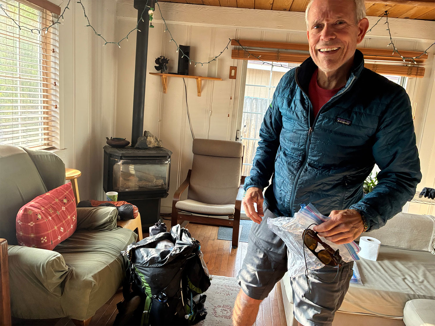 Hugh Safford, wearing outdoor gear, smiles in a cabin with a woodstove in the corner