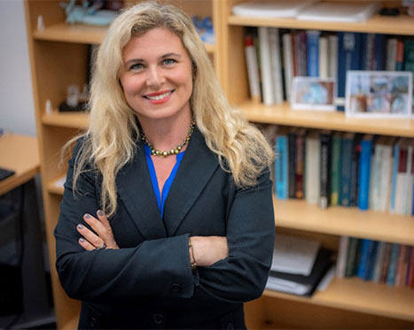 Rachel Whitmer crosses her arms over her chest and smiles at the camera in front of a bookshelf