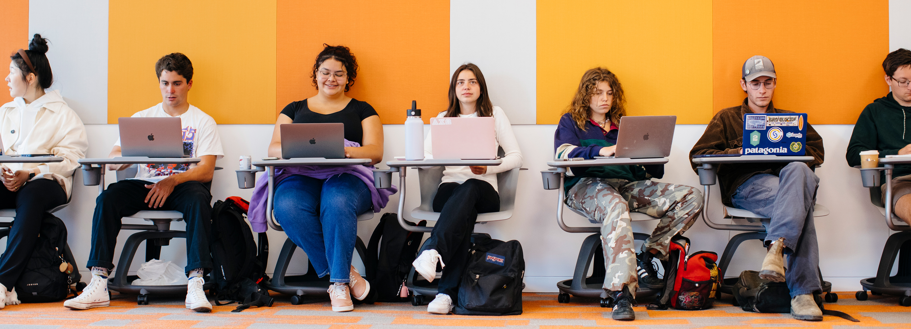 A row of students on laptops sitting at desks in a classroom