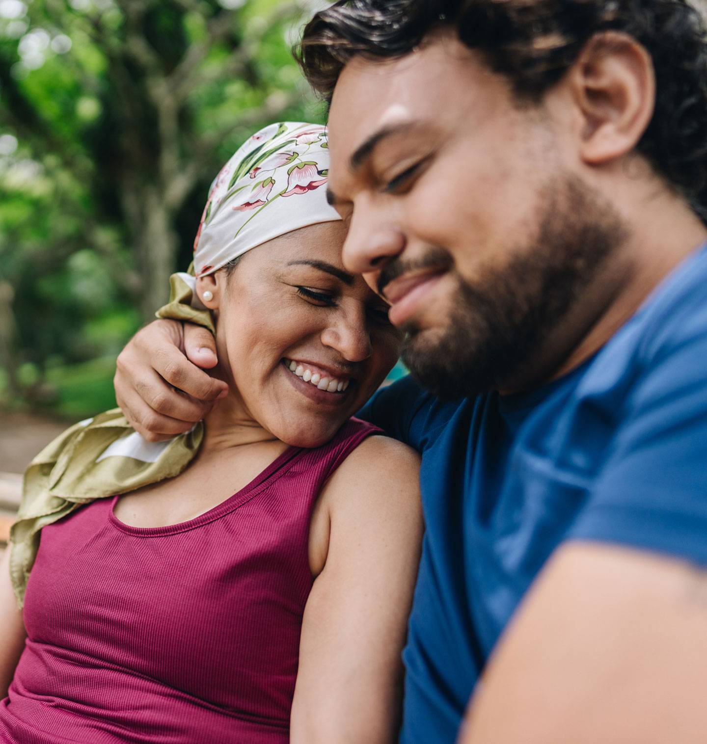 A smiling woman wearing a floral headscarf sits closely next to a man outdoors.