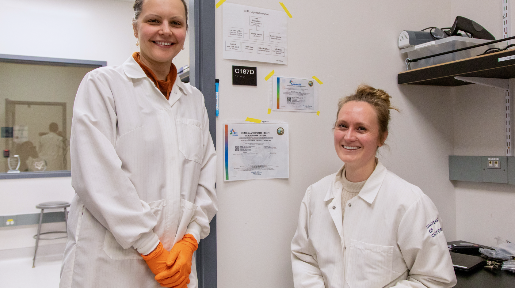 Two researchers wearing lab coats and brightly colored gloves