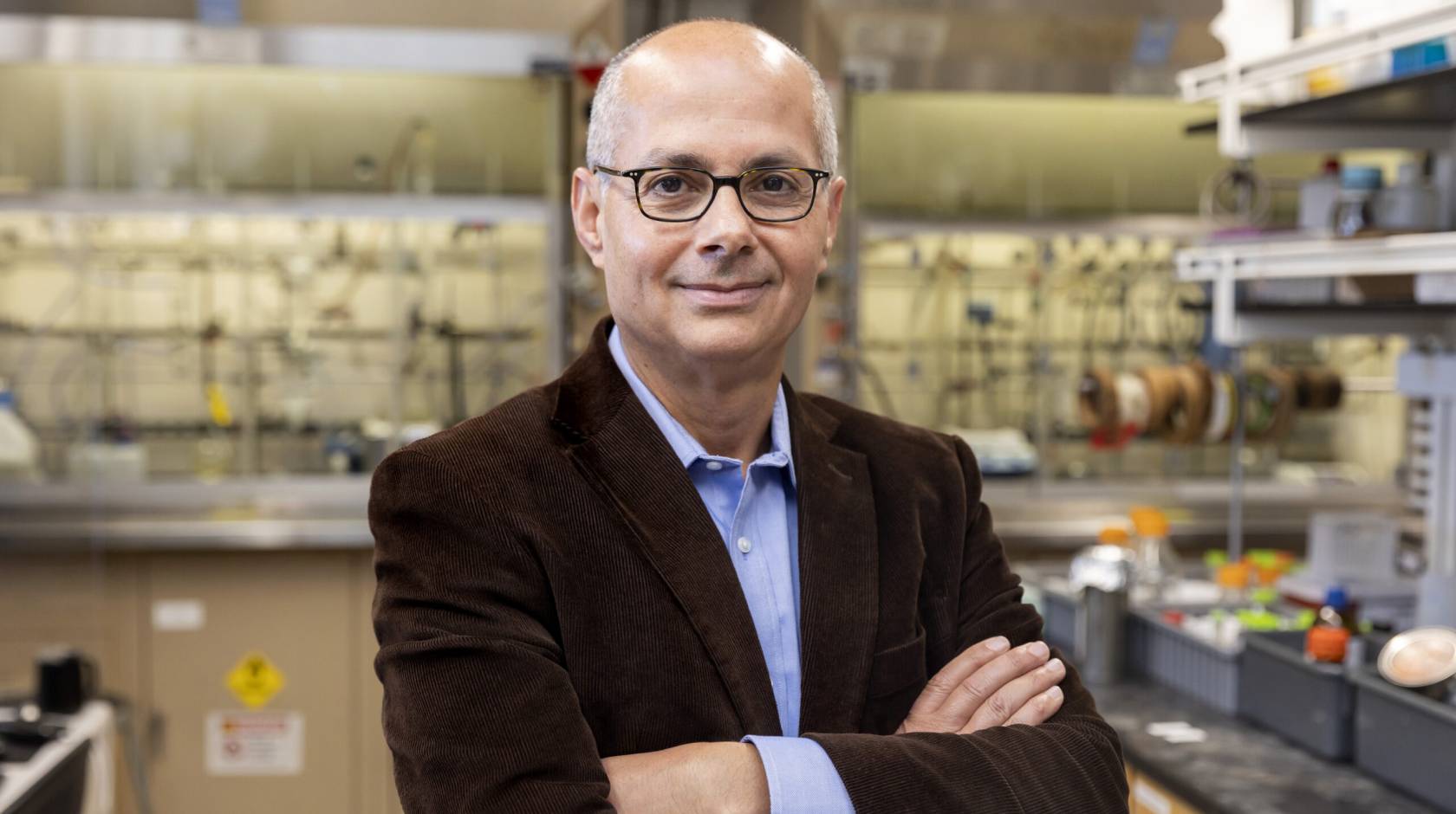A man with glasses in a brown jacket smiles at the camera in a lab (Omar Yaghi)