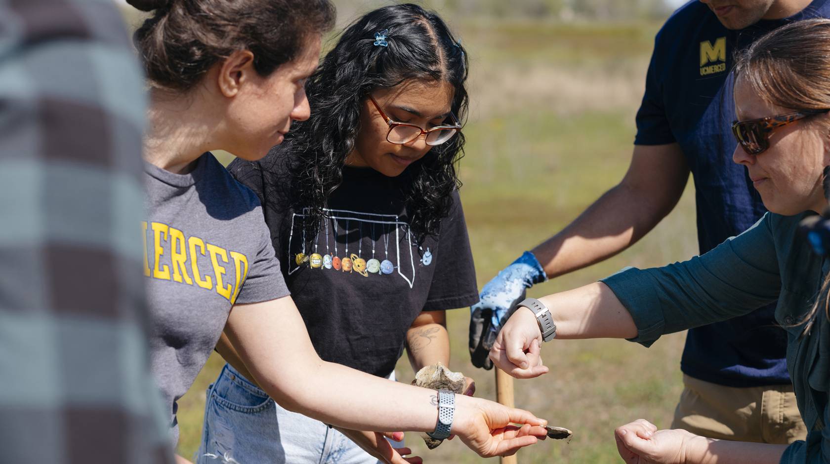 A group of people in a field, one is holding a rock they are all looking at