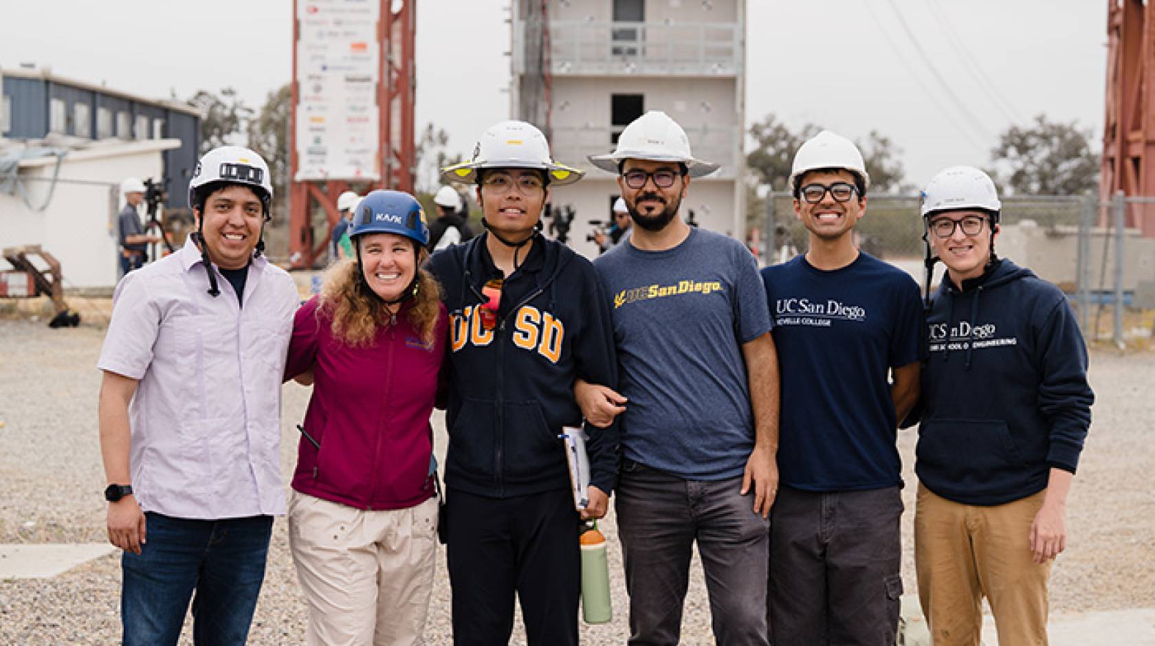 A group of engineers in hard hats stand in front of the earthquake simulator