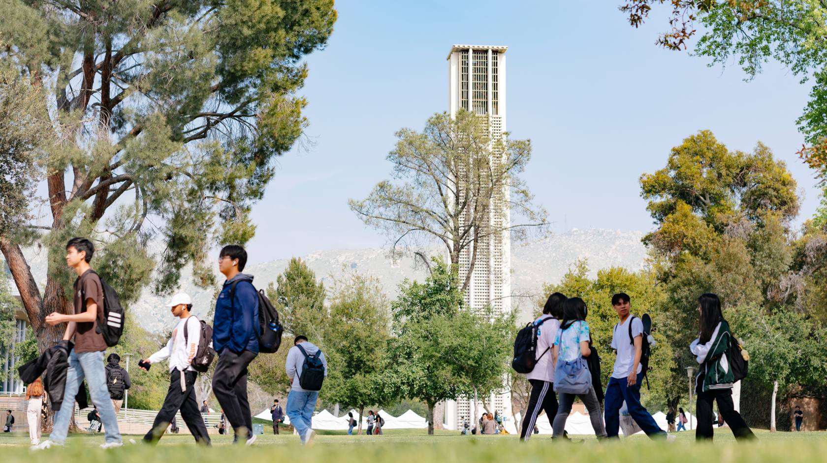 The UC Riverside Bell Tower seen through trees across campus, with students walking in the foreground