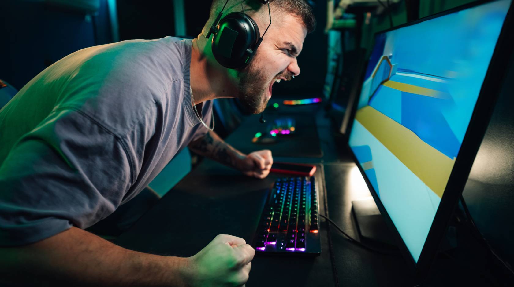 A man wearing headphones and at a keyboard screams at a computer monitor