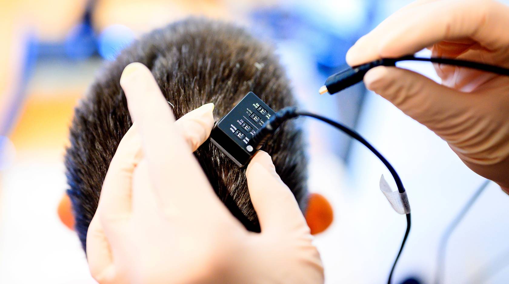 A close-up view of a pair of hands holding a small device about to be plugged in over someone's head