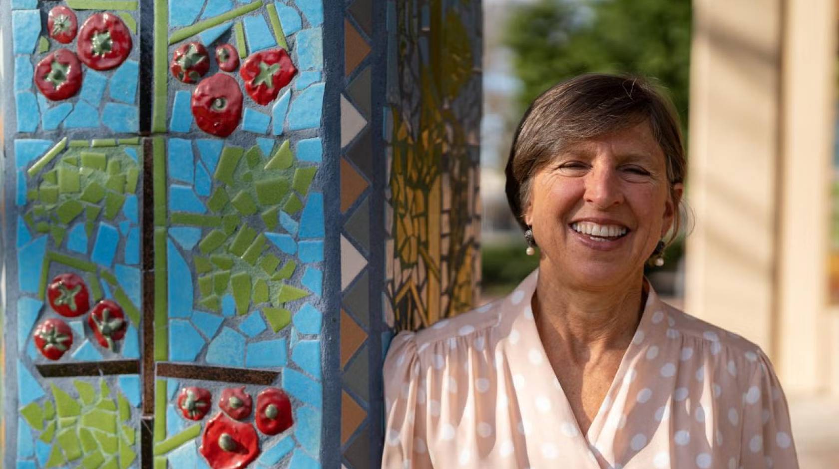 Woman smiles next to an outdoor pillar with a tomato mosaic