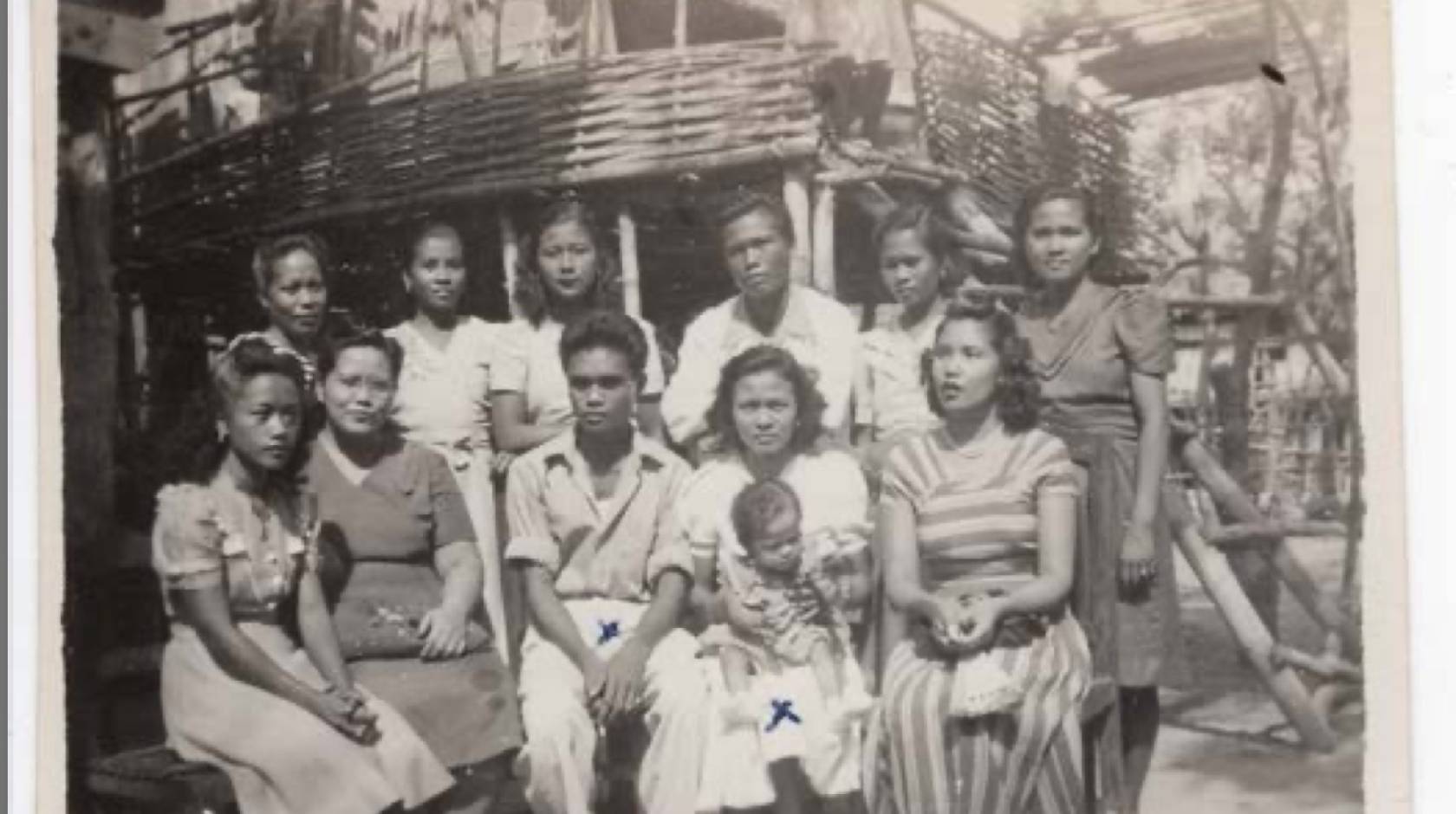 In an old black-and-white photo, a family poses outside