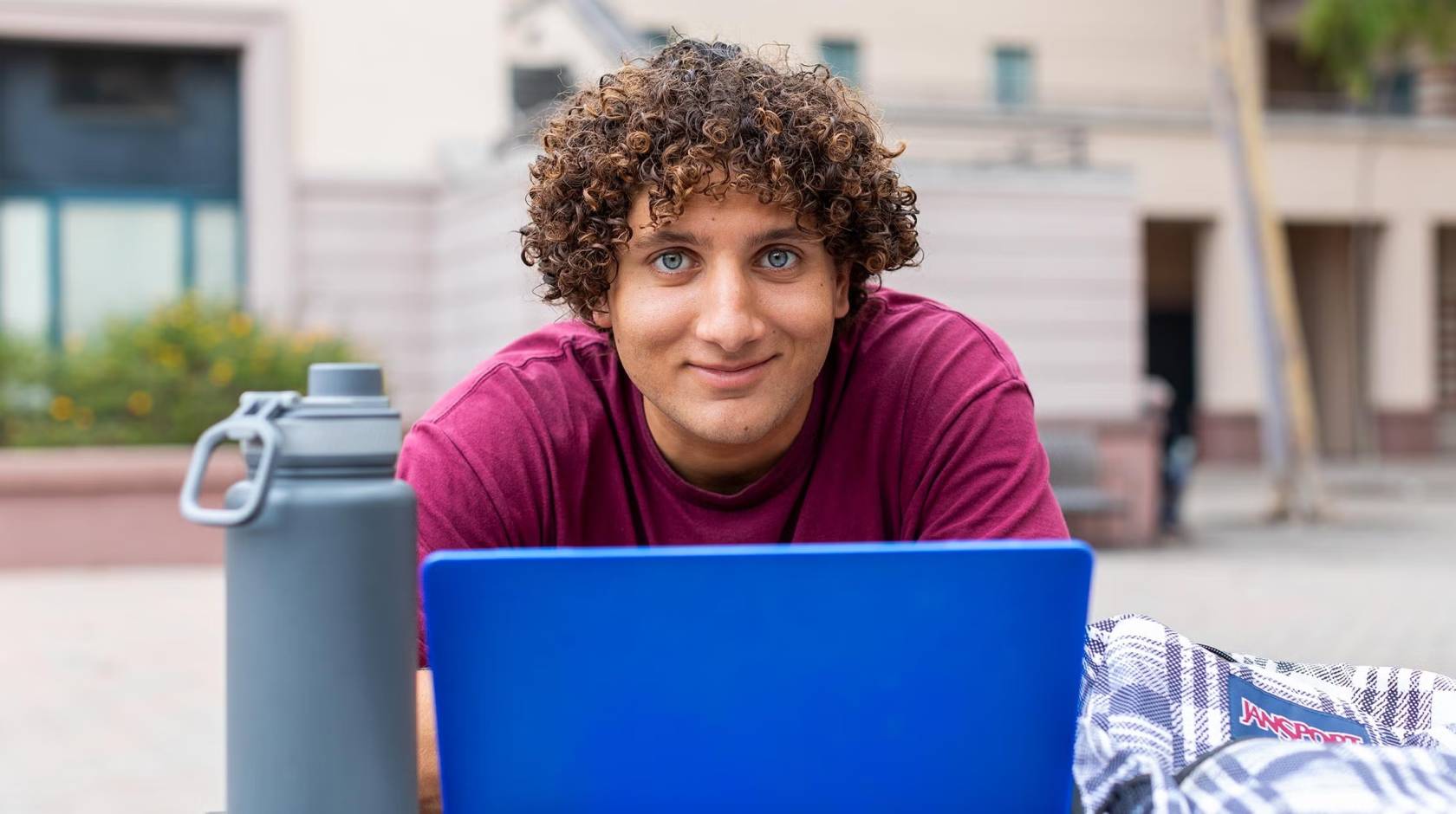 A young man with curly hair stares intently above a laptop while sitting outdoors