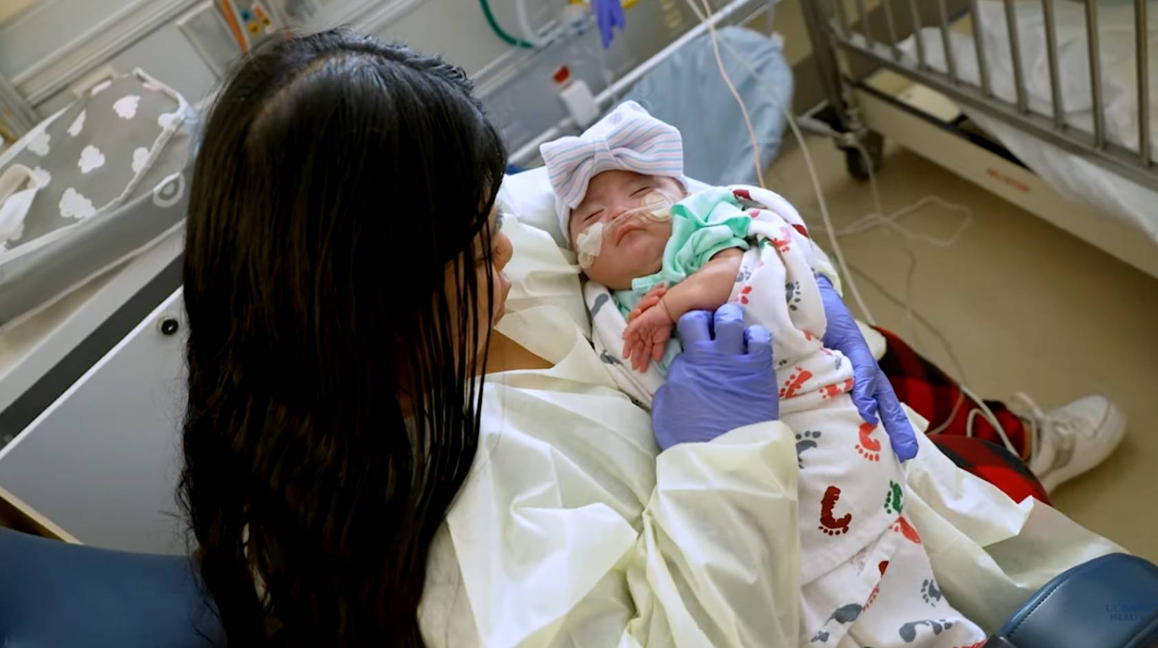 A young woman holds a young baby in her lap at a hospital