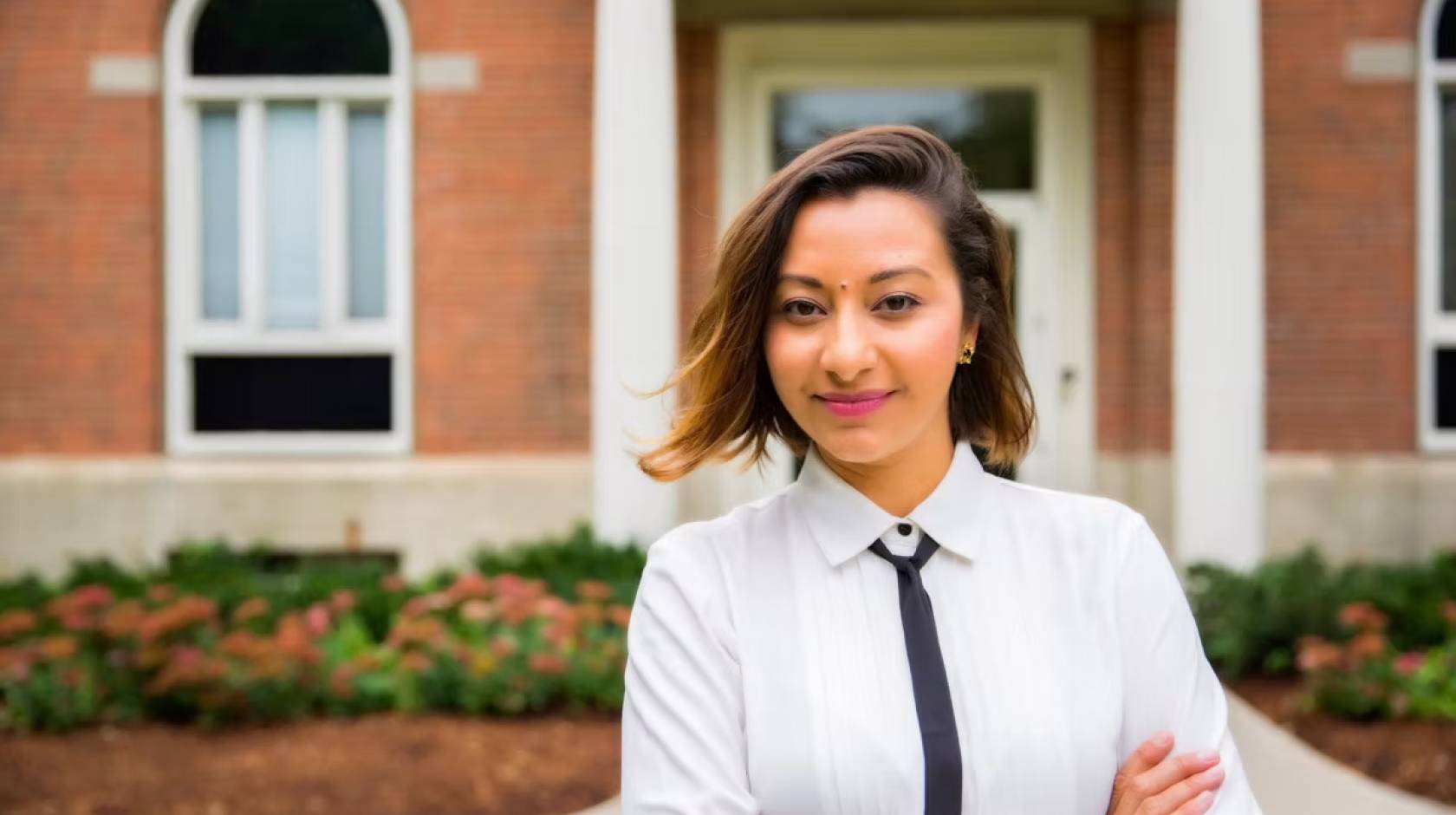 A woman with a skinny tie and arms crossed smiles at camera