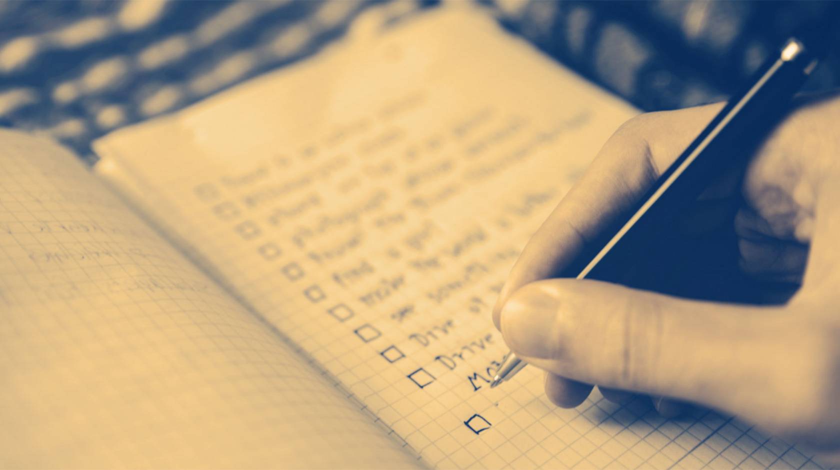 A sepia-toned close-up of a hand writing a to-do list with check-off boxes
