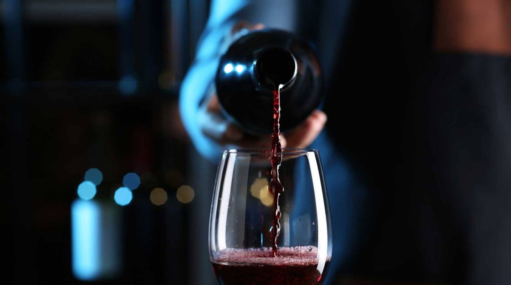 A hand pours a bottle of red wine into a wine glass, centered