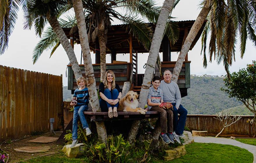 A family of four, with a golden retriever, sits together in a treehouse
