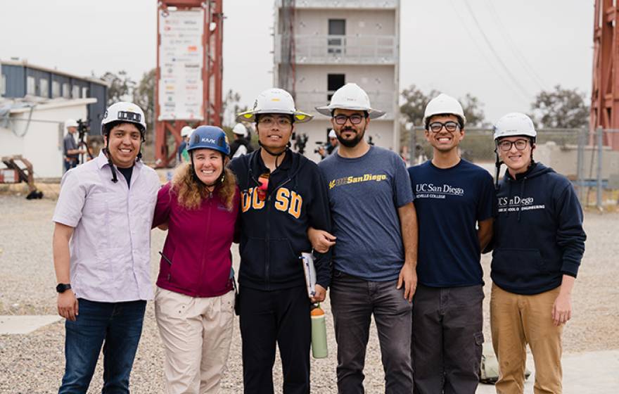 A group of engineers in hard hats stand in front of the earthquake simulator