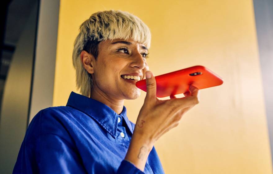 A young woman with a distinctive haircut speaks into a smart phone, smiling