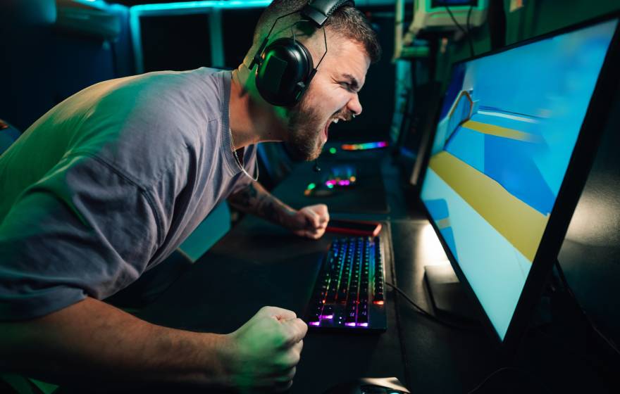 A man wearing headphones and at a keyboard screams at a computer monitor