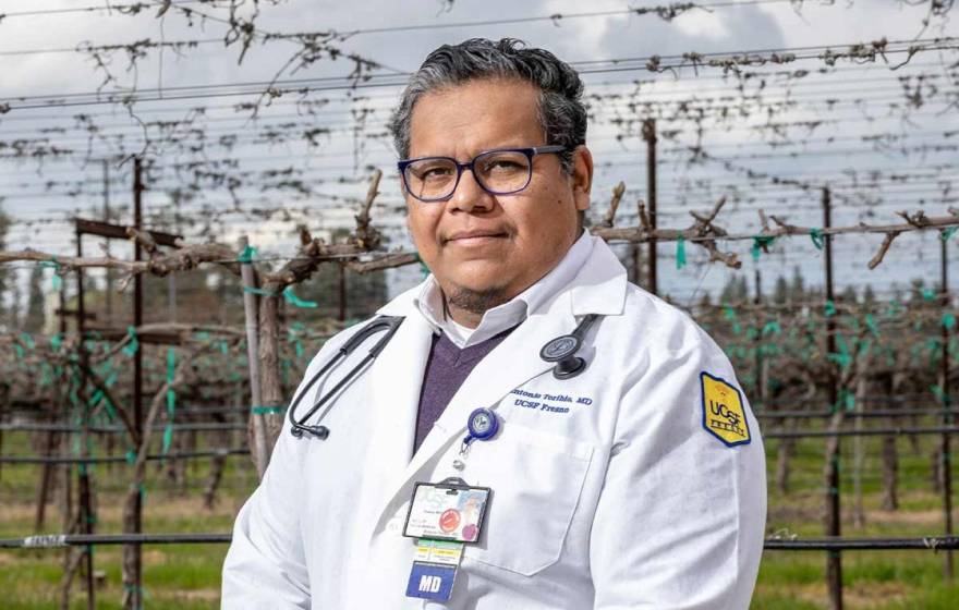 Doctor with dark gray hair and a medical coat stands in front of a vineyard