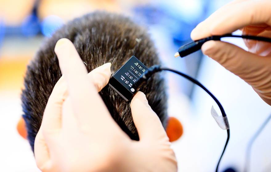 A close-up view of a pair of hands holding a small device about to be plugged in over someone's head