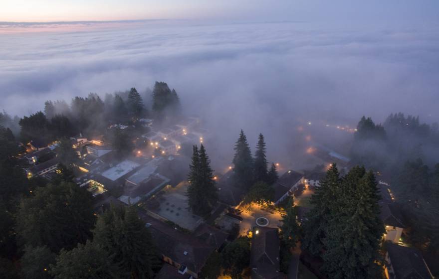 A view from above of heavy fog rolling from a reddish sky over a twilit UC Santa Cruz campus