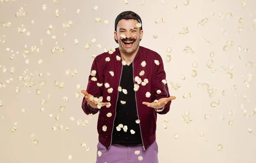 Laughing man in magneta jacket and mustache while pasta chips fall around him