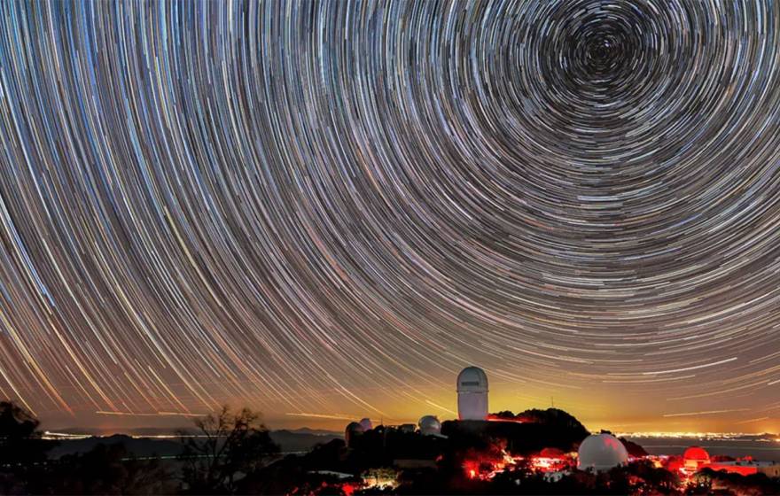 A telescope on a mountain peak at sunset, taken using time lapse to show concentric circles of star trails in the sky