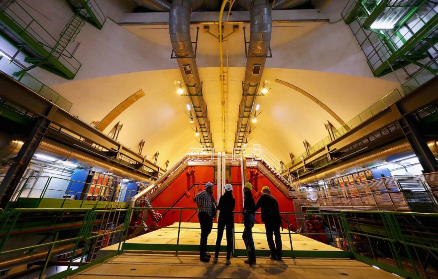 Four people stand backlit in a giant room full of high-tech machinery
