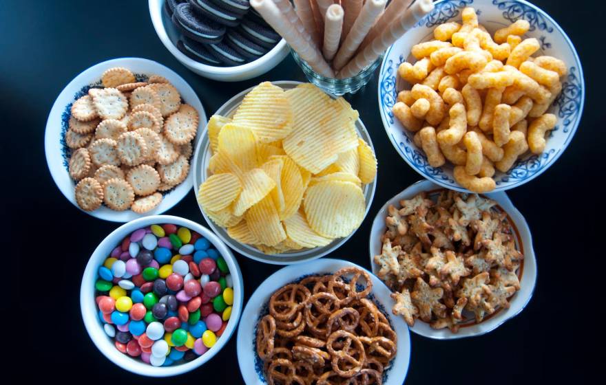 8 small bowls and a glass full of chips, pretzels, cookies and other processed foods
