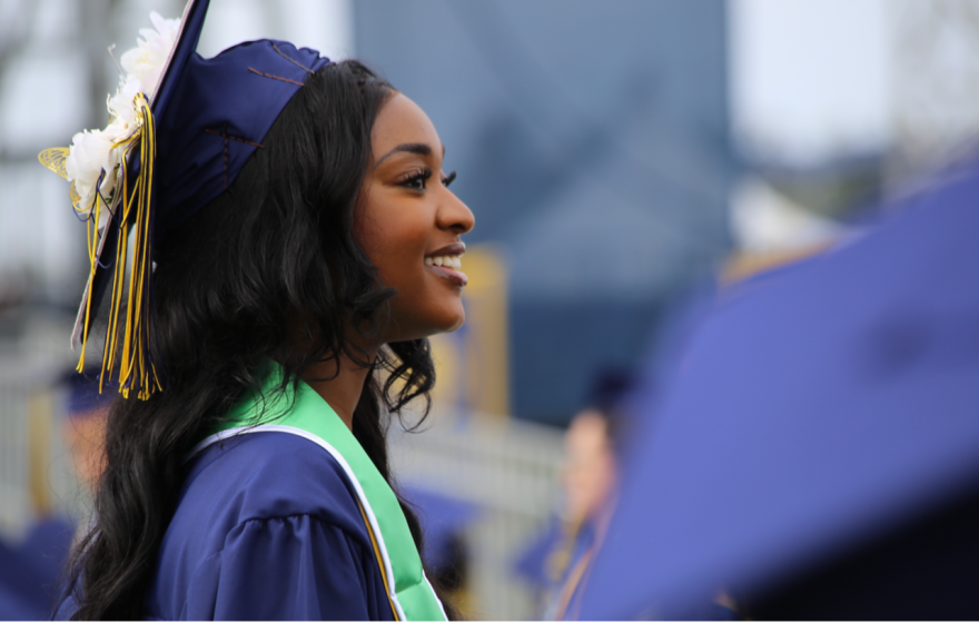 A young woman in a cap, gown and stole looks on happily during a graduation ceremony